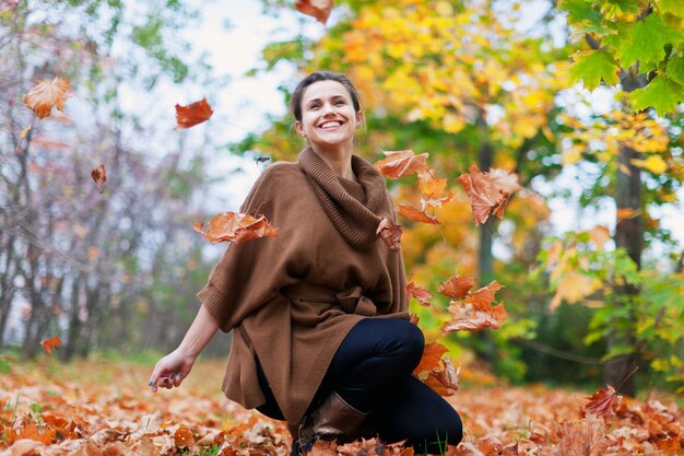 La muchacha feliz lanza las hojas de arce