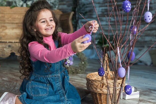 Muchacha feliz que cuelga los huevos de Pascua en rama