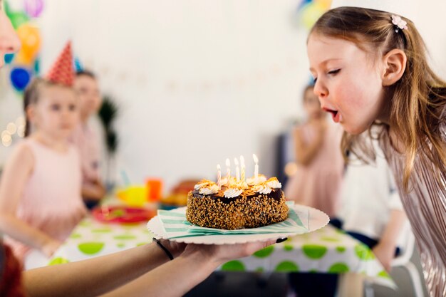 Muchacha feliz que sopla velas en la torta