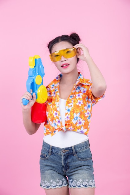 Foto gratuita muchacha feliz que sostiene un arma de agua rosado del fondo.