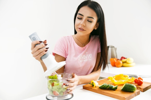 La muchacha hace una bebida sana con el mezclador en la cocina