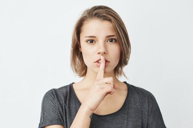 La muchacha hermosa joven en la camiseta gris que muestra guarda silencio.