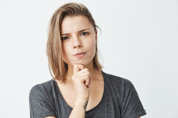 Muchacha hermosa joven que piensa con la mano en la barbilla que frunce el ceño.