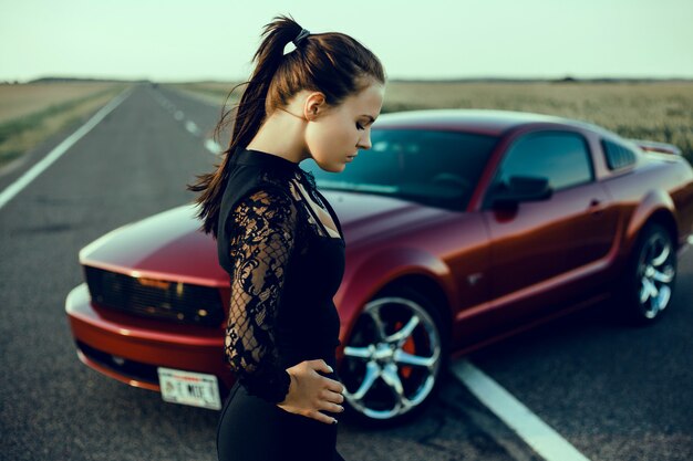 Muchacha hermosa joven que presenta cerca del coche rojo costoso, coche potente