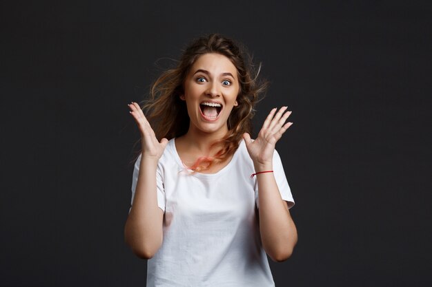 Muchacha hermosa joven que sonríe regocijo sobre la pared gris.