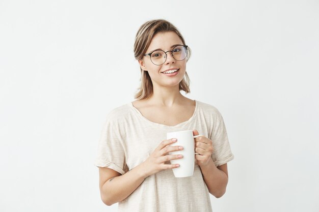 Muchacha hermosa linda en vidrios que sonríe sosteniendo la taza.