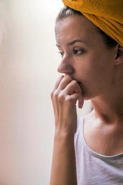 Muchacha hermosa que se coloca en la ventana que mira. Hermosa niña triste solitaria sentada cerca de la ventana falta