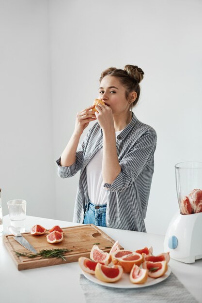 Muchacha hermosa que come el pedazo del pomelo sobre la pared blanca. Nutrición saludable y saludable. Copia espacio