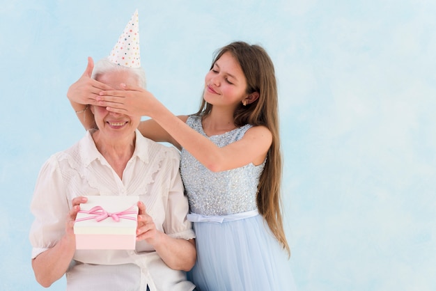 Muchacha hermosa que da el regalo sorprendido cubriendo los ojos de su abuela