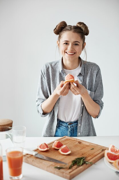 Muchacha hermosa que sonríe llevando a cabo el pedazo del pomelo sobre la pared blanca. Nutrición saludable y saludable.