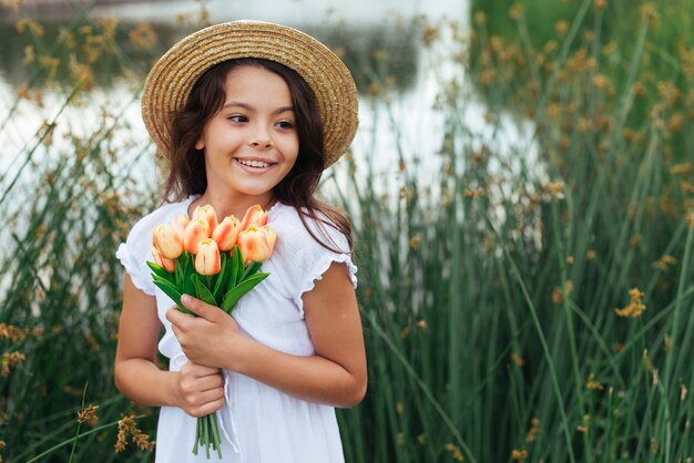 Muchacha hermosa que sostiene las flores por el lago