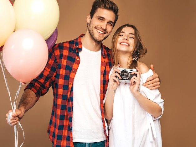 Muchacha hermosa sonriente y su novio hermoso que sostiene el manojo de globos coloridos. Feliz pareja tomando foto selfie de sí mismos en la cámara retro. Feliz cumpleaños