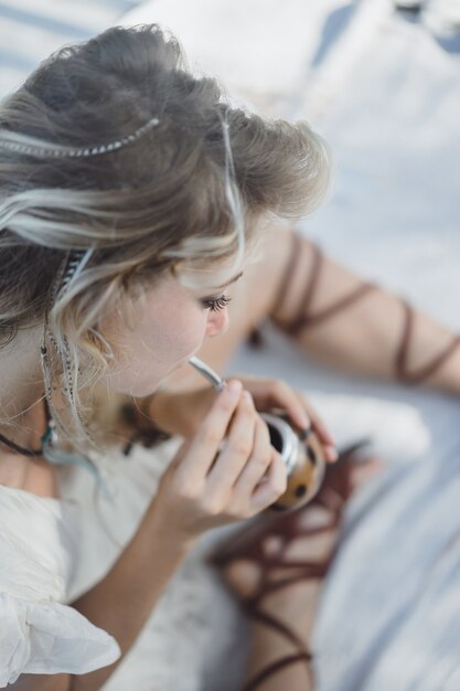 Muchacha india hermosa del hippie con el pelo rubio largo en el té de consumición del compañero del tejado.