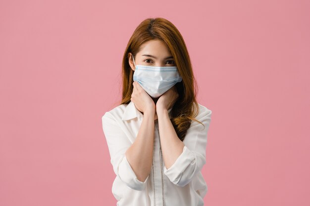 La muchacha joven de Asia usa una mascarilla médica, cansada del estrés y la tensión, mira con confianza a la cámara aislada sobre fondo rosa.