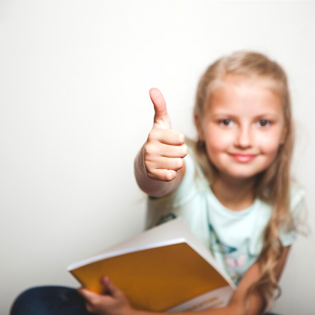 Muchacha con el libro que da el pulgar para arriba que sonríe