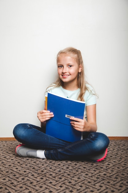 Muchacha con los libros de ejercicio que se sientan en suelo