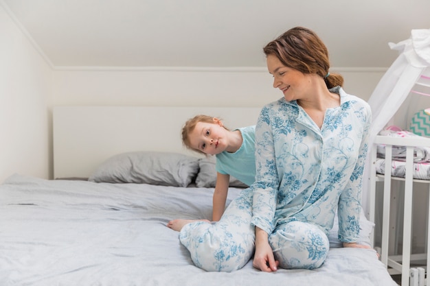 Muchacha linda sonriente que se divierte con su madre en cama