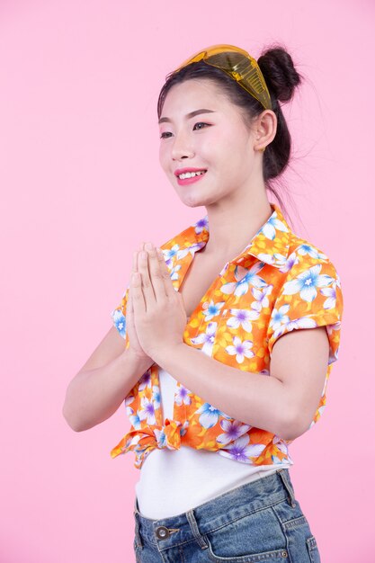 La muchacha de la moda se viste para arriba con gestos de mano en un fondo rosado.