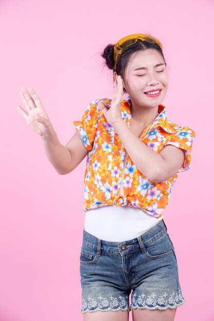 La muchacha de la moda se viste para arriba con gestos de mano en un fondo rosado.