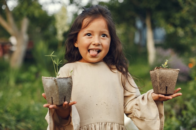 Muchacha del niño que sostiene una plántula lista para ser plantada en el suelo. Jardinero pequeño con un vestido marrón.