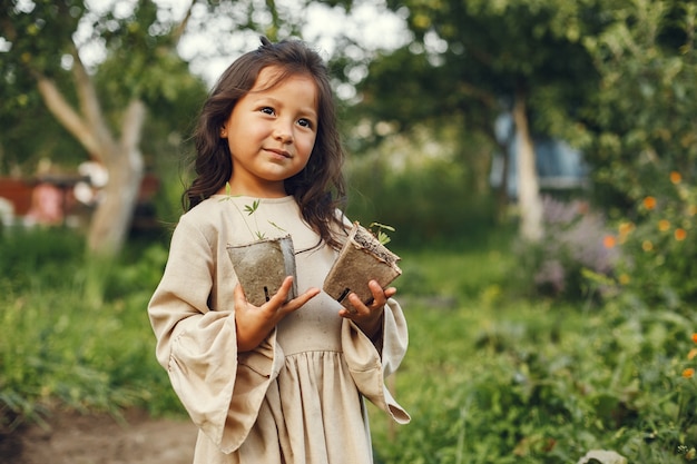 Muchacha del niño que sostiene una plántula lista para ser plantada en el suelo. Jardinero pequeño con un vestido marrón.