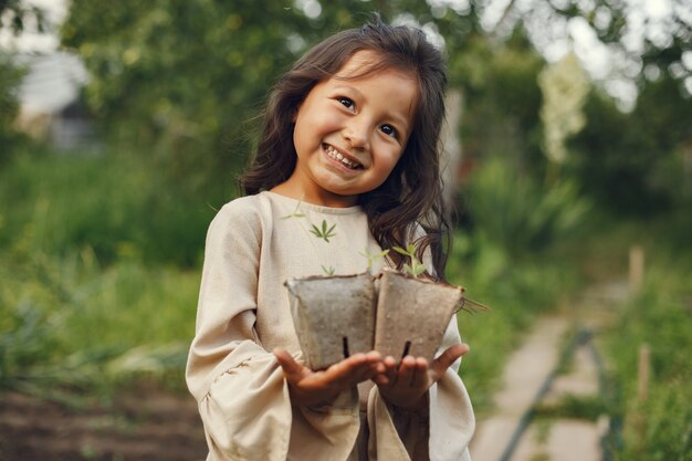 Muchacha del niño que sostiene una plántula lista para ser plantada en el suelo. Jardinero pequeño con un vestido marrón.