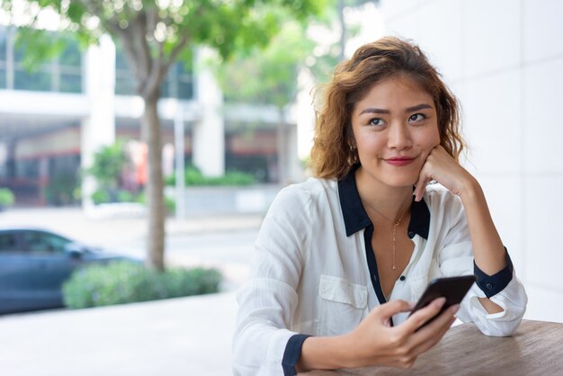 Muchacha de oficina asiática positiva que descansa en café de la calle