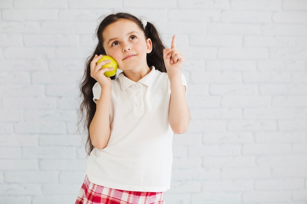 Foto gratuita muchacha de pie sosteniendo la manzana apuntando hacia arriba