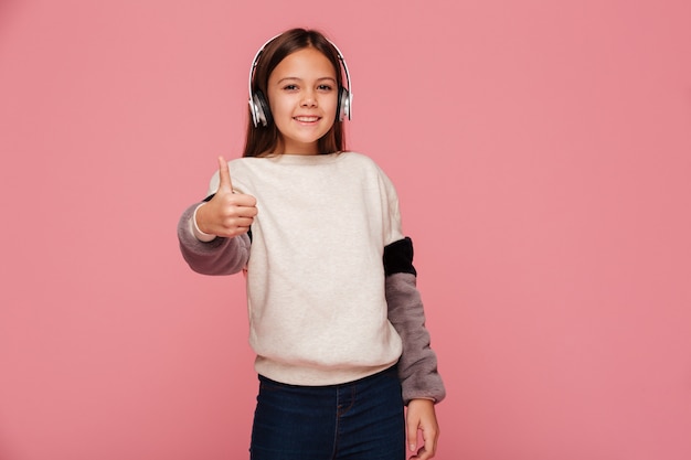 Foto gratuita muchacha positiva alegre en los auriculares que muestran el pulgar para arriba aislado