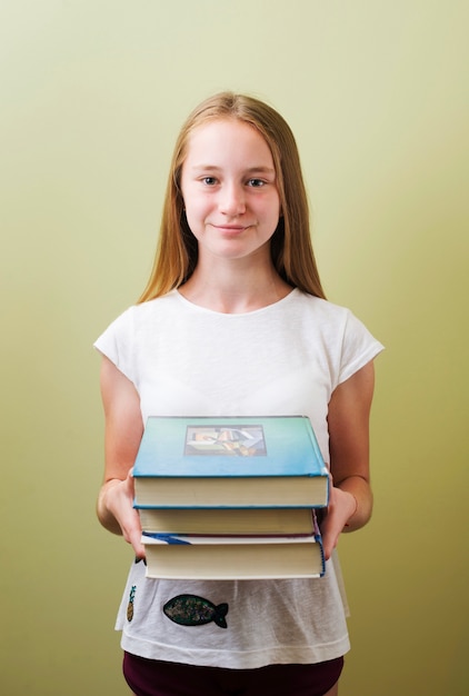 Muchacha que se coloca con la pila de libros