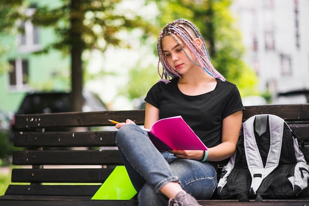 Muchacha que estudia en banco en parque