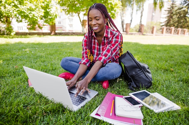 Muchacha que estudia con la computadora portátil en parque