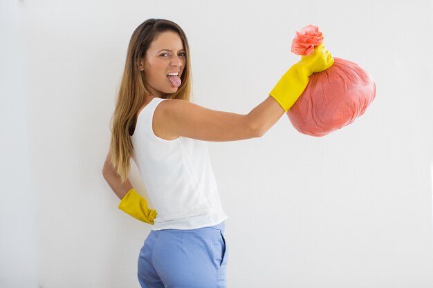 Muchacha que hace muecas con el bolso de basura que pega la lengüeta hacia fuera