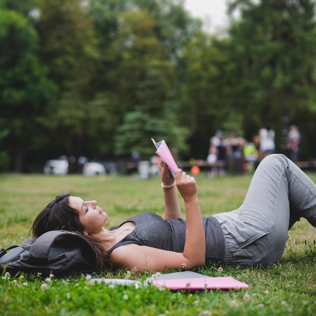 Muchacha que miente en hierba en la lectura del parque