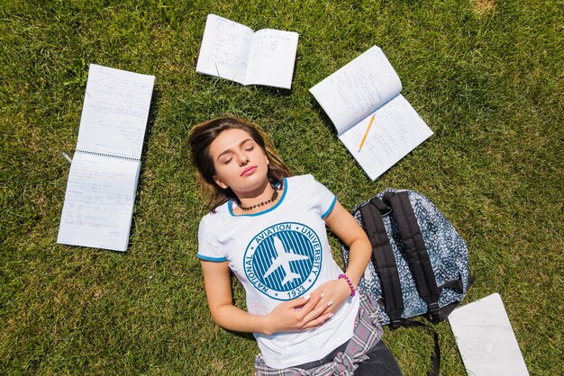 Muchacha que miente en hierba rodeada por los cuadernos