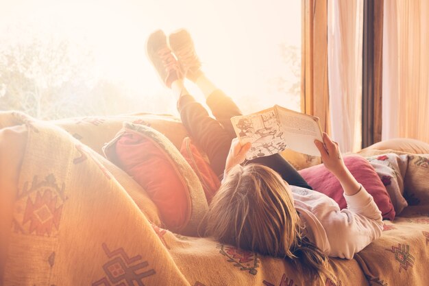 Muchacha que miente en el libro de lectura del sofá