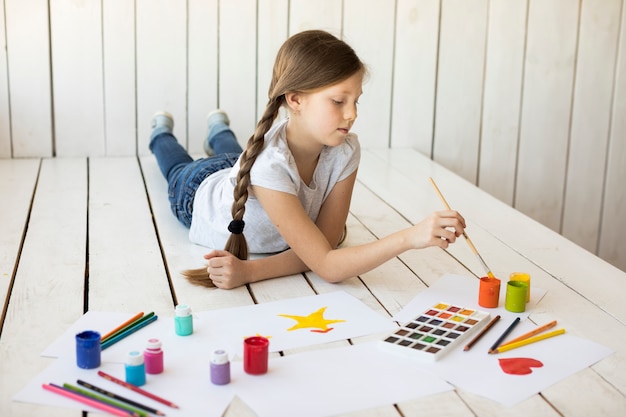 Muchacha que miente en la pintura del piso de madera dura en el papel con la brocha