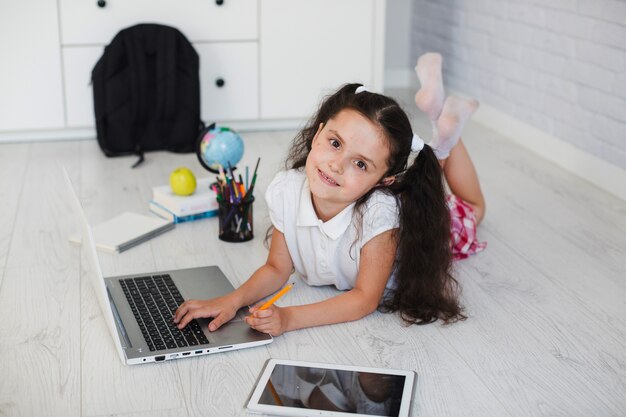 Muchacha que miente en el suelo que toca la computadora portátil