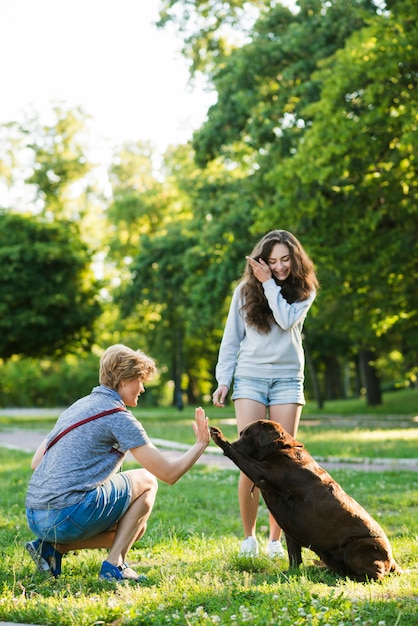 Muchacha que mira a la mujer que da el alto cinco a su perro en parque