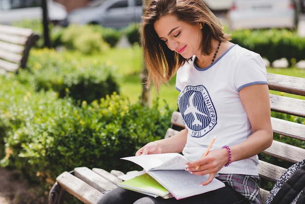 Muchacha que se sienta en el banco que sostiene los cuadernos que estudian