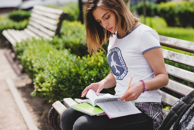 Muchacha que se sienta en el banco que sostiene los cuadernos que estudian