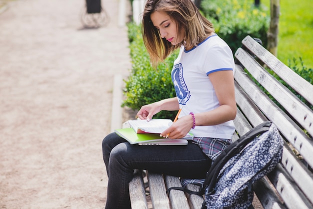 Muchacha que se sienta en el banco que sostiene los cuadernos que estudian