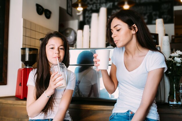 Muchacha que se sienta en el café que sostiene las tazas que beben