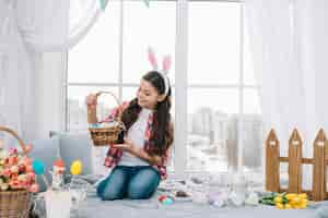 Foto gratuita muchacha que se sienta en la cama que mira la cesta de los huevos de pascua en casa