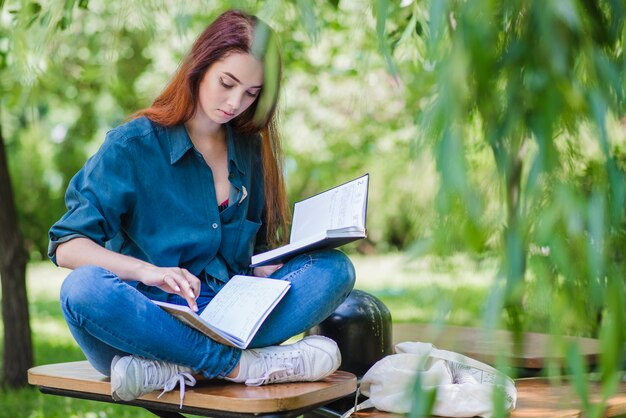 Muchacha que se sienta en libro de explotación del parque que lee