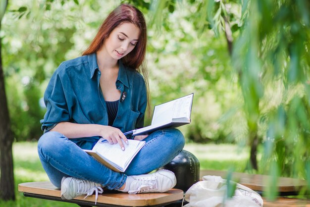 Muchacha que se sienta en libro de explotación del parque que lee