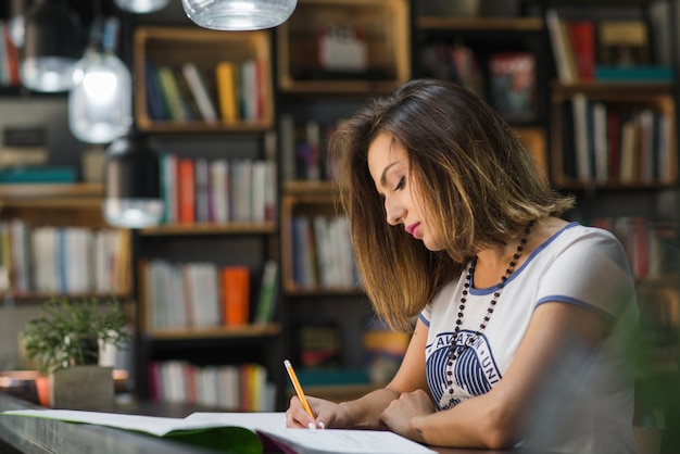 Muchacha que se sienta en la mesa con los cuadernos que escriben