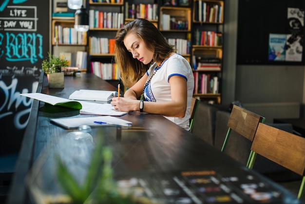 Muchacha que se sienta en la mesa con los cuadernos que escriben