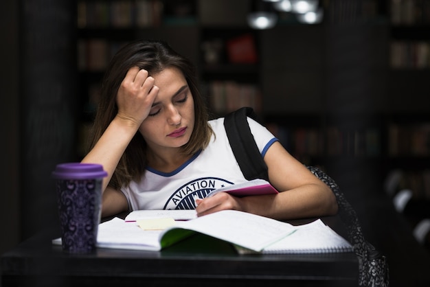 Foto gratuita muchacha que se sienta en la tabla con la lectura de los cuadernos