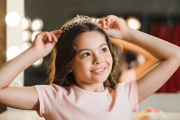 Muchacha que soña despierto que sostiene la corona en su cabeza que mira lejos